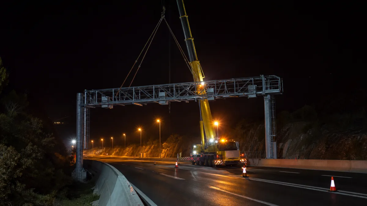 Ein Technikportal wird nachts mit einem Kran über einer Autobahn montiert