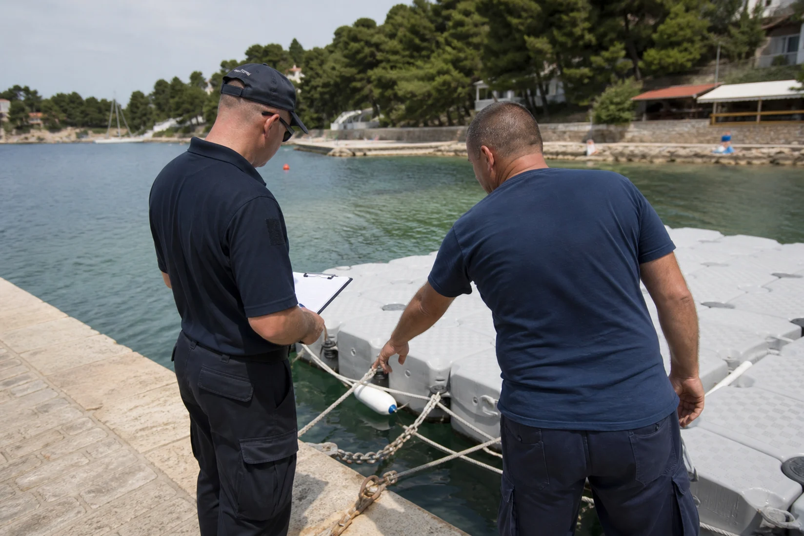 Zwei Mitarbeiter prüfen Befestigungen eines leeren schwimmenden Pontons an einer Adriabucht