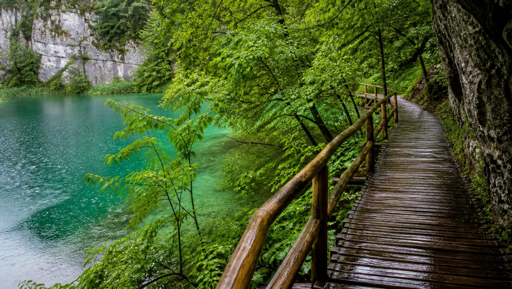 Nasser Holzsteg an einem grünblauen See im Nationalpark Plitvice