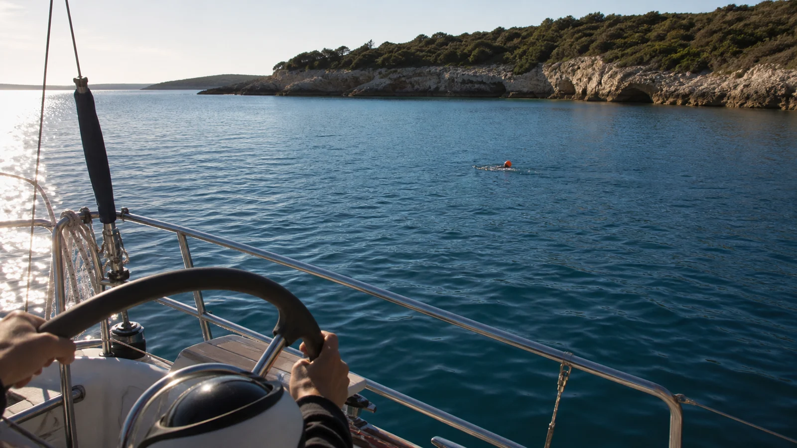 Ein Schwimmer mit heller Kappe und Sichtboje wirkt vom Cockpit einer Segelyacht sehr klein
