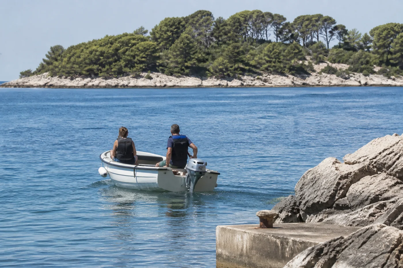 Zwei Personen mit Rettungswesten fahren langsam mit einem kleinen Motorboot aus einer dalmatinischen Bucht