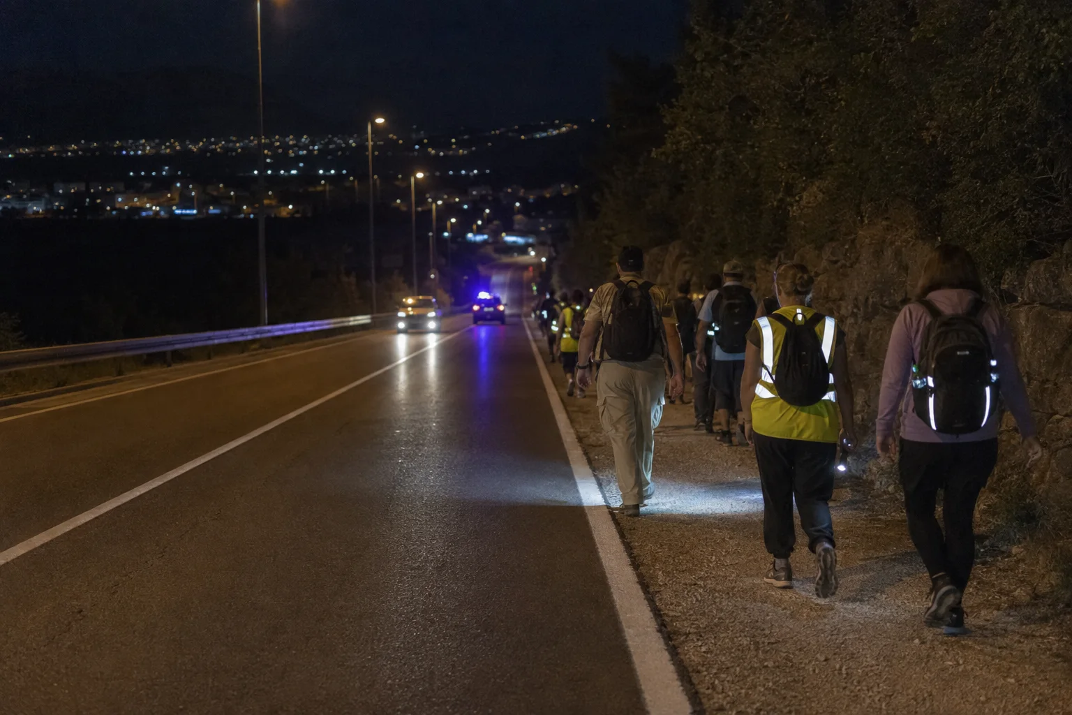 Pilger gehen nachts mit reflektierenden Westen und Lampen am Rand einer Straße