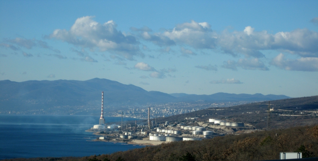 Panoramablick auf die Raffinerie Rijeka am Standort Urinj mit Tanks, Anlagen und Schornstein an der Küste