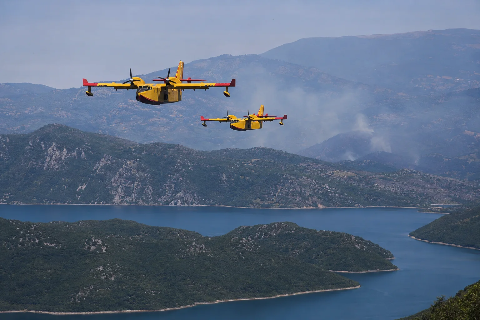 Zwei gelbe Löschflugzeuge fliegen über Berg- und Seenlandschaft in Bosnien-Herzegowina