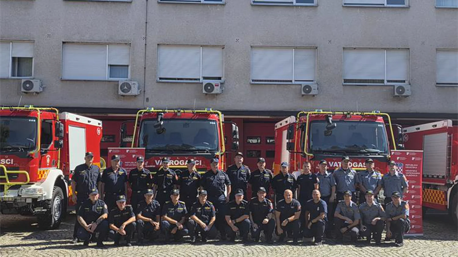 Kroatische Feuerwehrleute und Vertreter stehen bei der Übergabe vor mehreren roten Waldbrandfahrzeugen