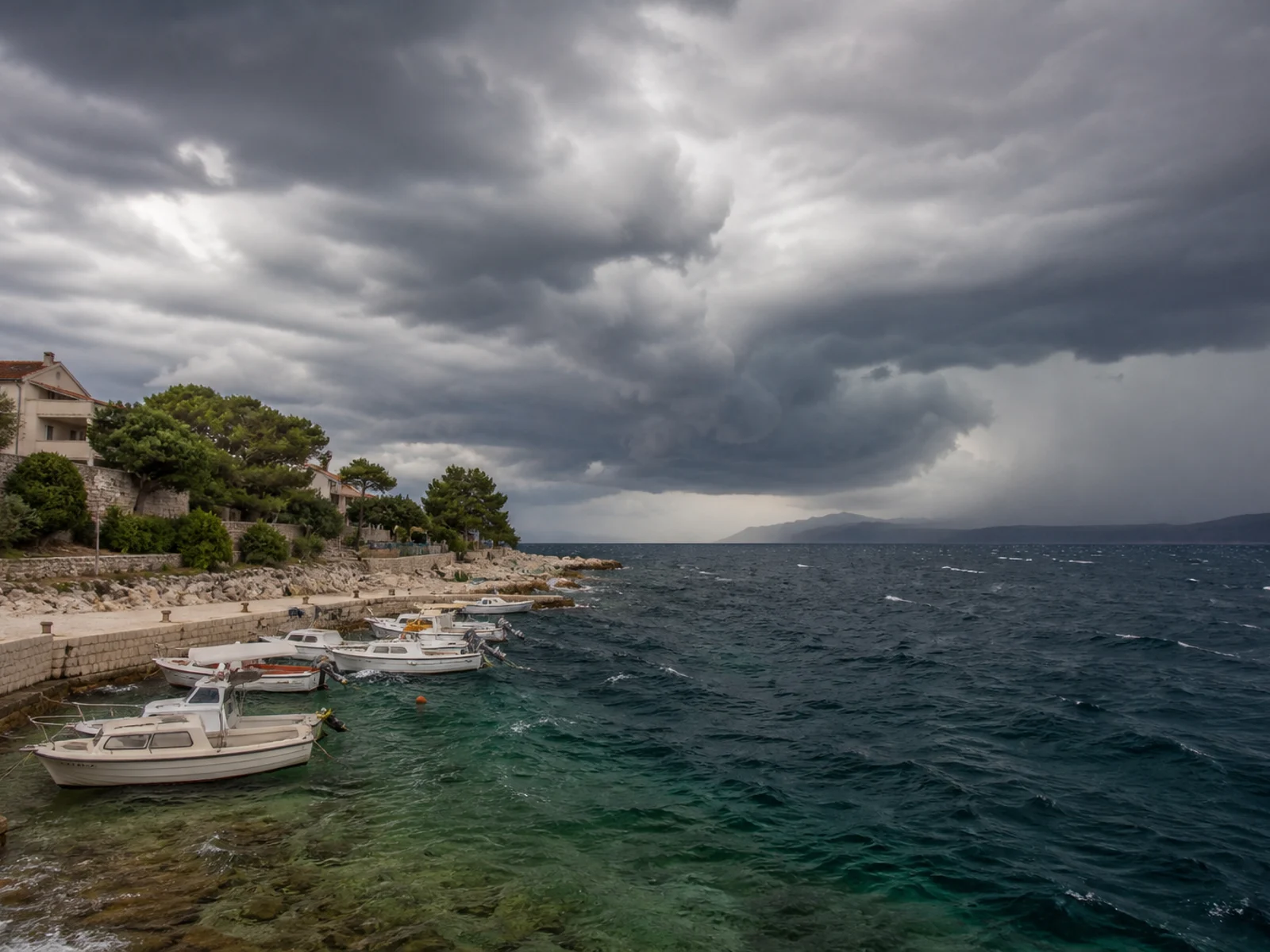 Dunkle Gewitterwolken über einem kroatischen Hafen mit gesicherten kleinen Booten