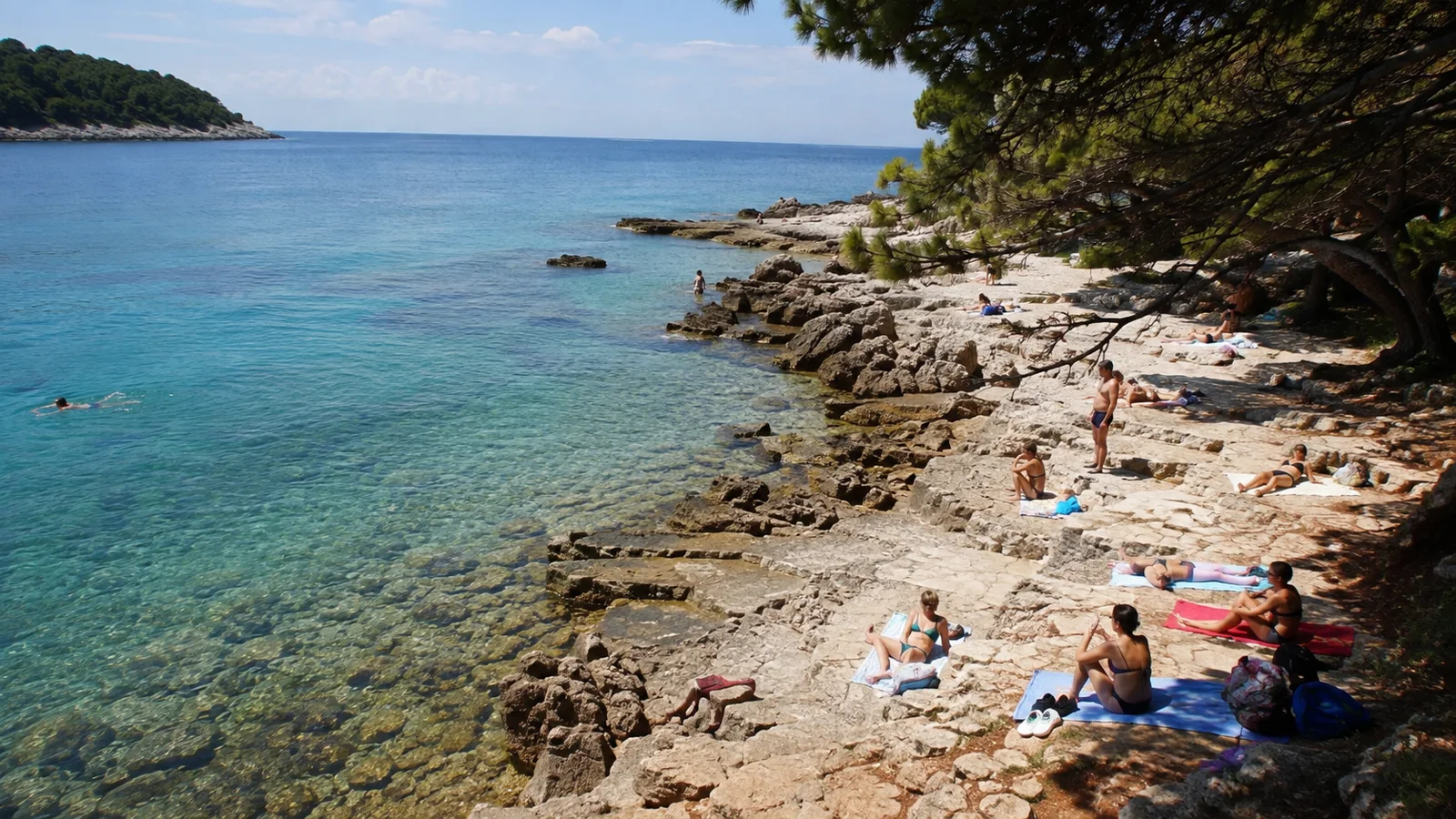 Erwachsene Badegäste in Badekleidung verteilen sich an einem natürlichen Felsstrand auf Lokrum
