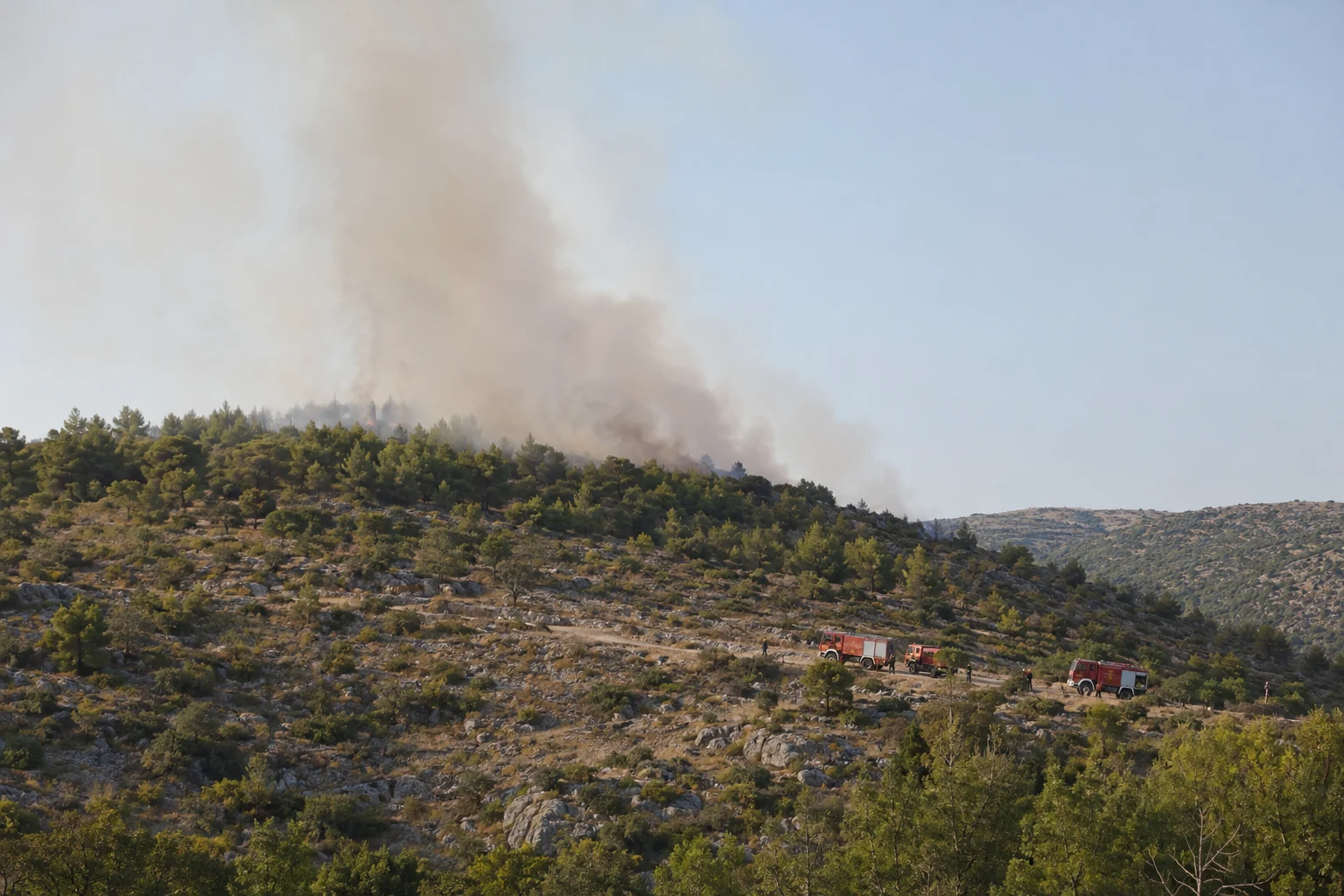 Feuerwehrkräfte beobachten einen Vegetationsbrand in einer felsigen Kiefernlandschaft Dalmatiens