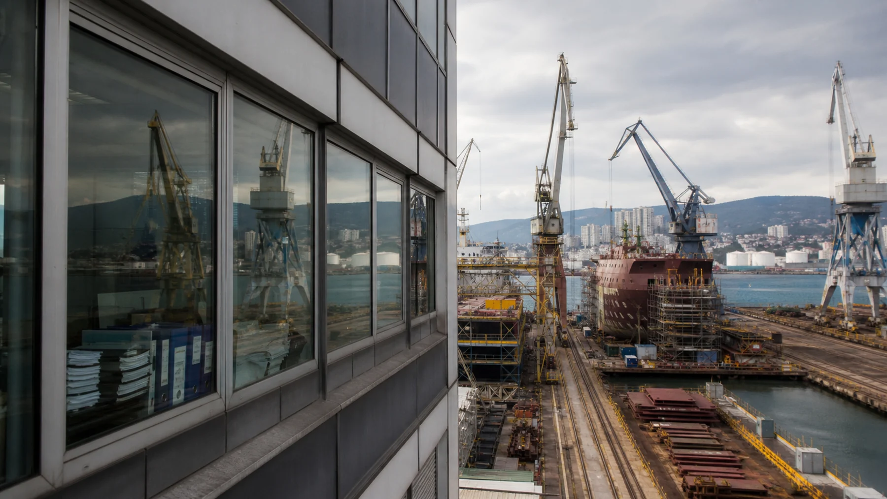 Blick aus einem Verwaltungsgebäude auf Kräne und einen Schiffsrumpf in einer Werft am Kvarner