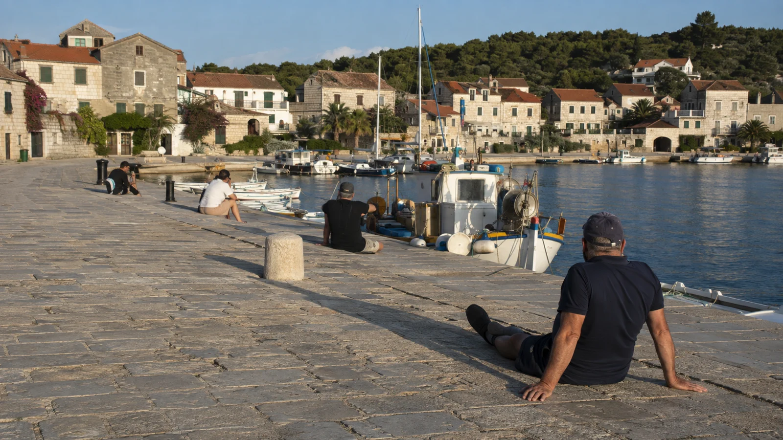 Bewohner und Besucher ruhen auf der Linčarnica am Hafen von Sali und schauen auf die Boote