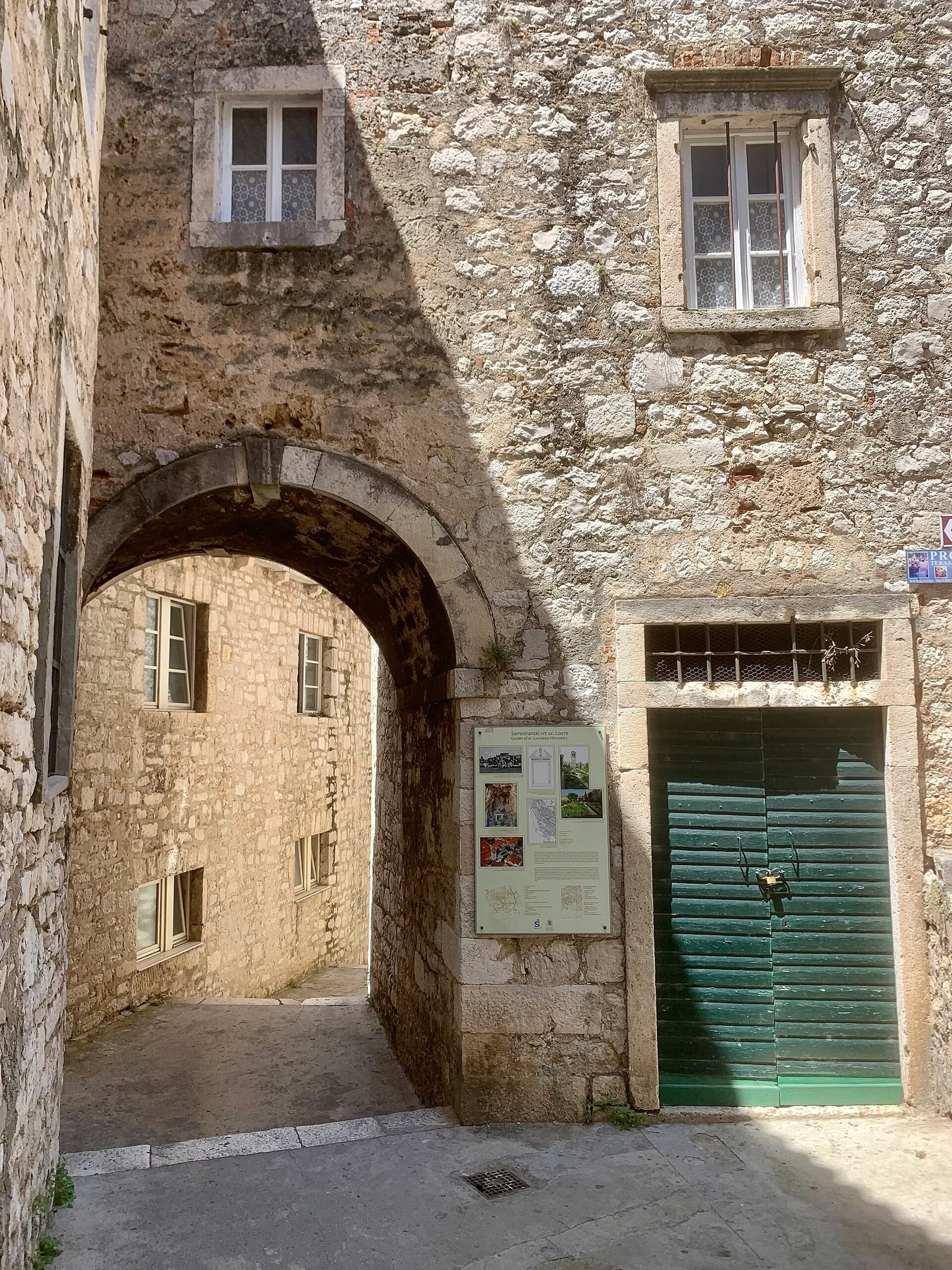 Steinerne Altstadtgasse mit Bogen und grünen Fensterläden in Šibenik