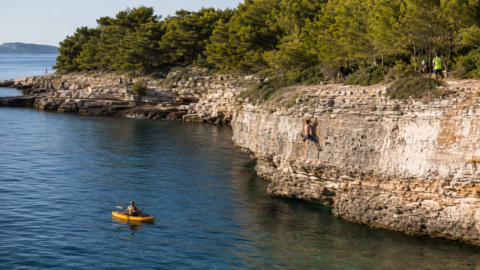 Ein Teilnehmer klettert über tiefem Wasser an der Punta Bajlo, ein Sicherungskajak wartet in der Bucht